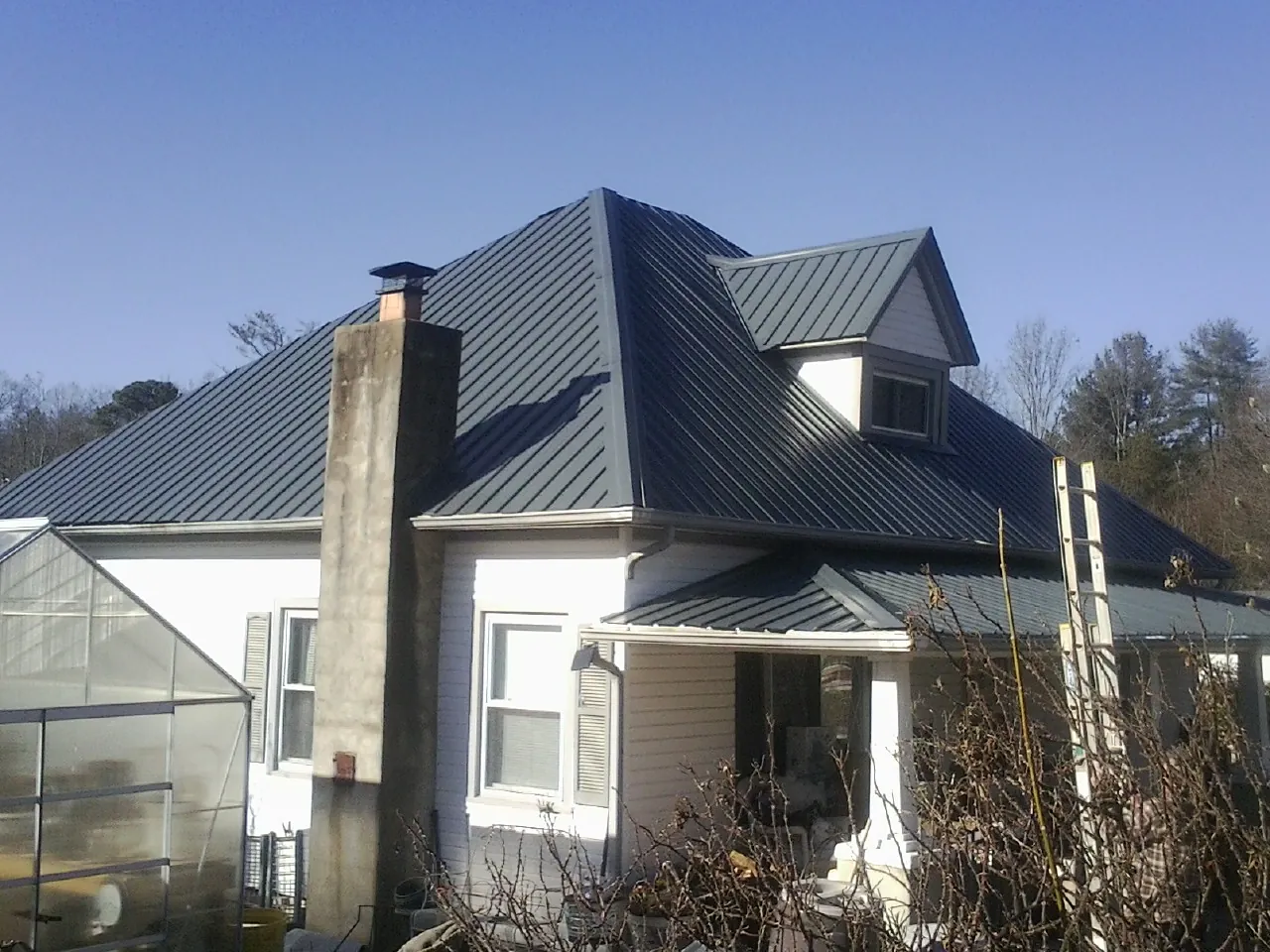 Dark blue standing seam metal roof on a white farmhouse with dormer — Slate & Tile Roof Repair by Roofing Brothers in Long Creek