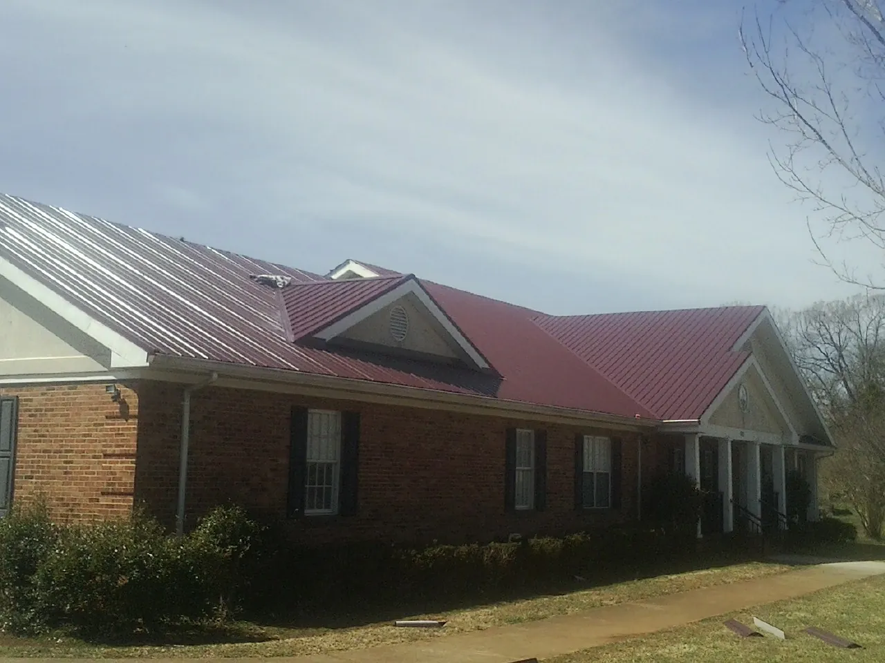 Red metal roof with gabled entries on a long brick building, from a Hail Damage Roof Repair job in Long Creek