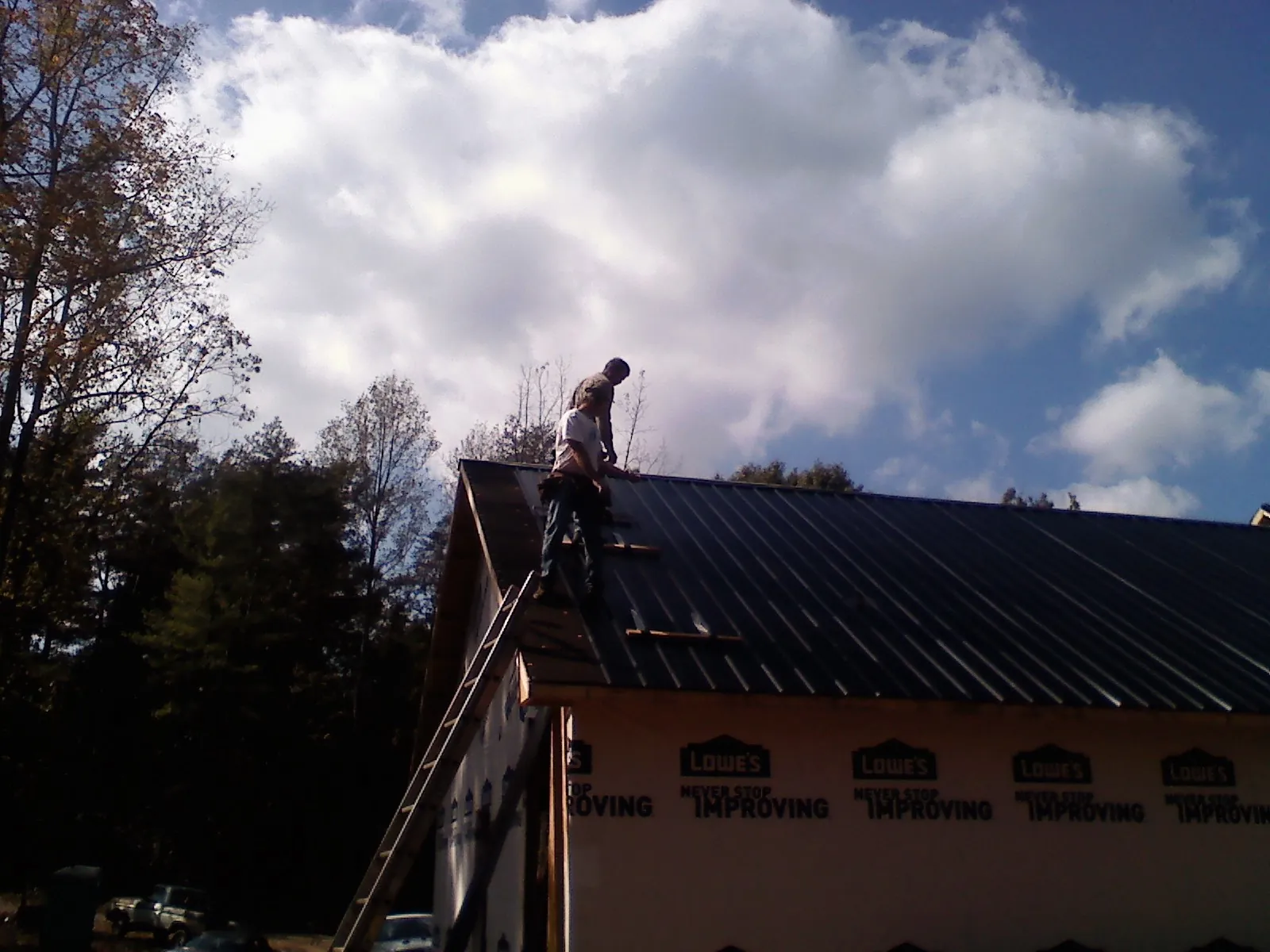 Roofer fastening dark metal panels high against a cloudy sky, from a Roof Inspection job in Long Creek
