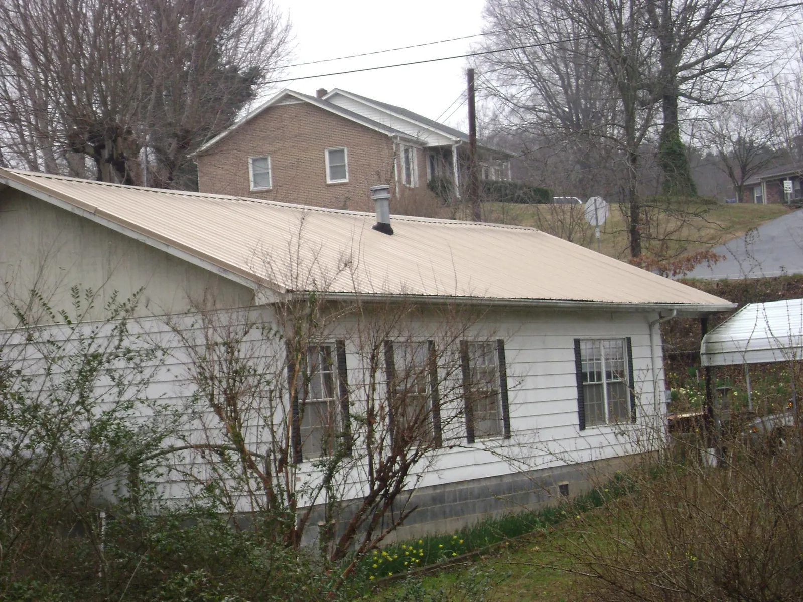 Tan metal roof on a white sided house set into a hillside — Commercial Roofing by Roofing Brothers in Long Creek